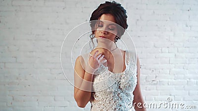 De zoete dame met donker haar in een zacht kapsel bevindt zich in de studio in een lange elegante witte kleding, het stellen, het stock footage De zoete dame met donker haar in een zacht kapsel bevindt zich in de studio in een lange elegante witte kleding, het stellen, het stock footage