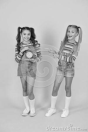 Dead line. Happy little girls hold vintage alarm clock on yellow background. Small children smiling with mechanical Stock Photo