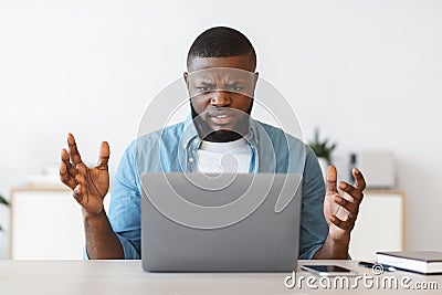 Deadline Stress. Annoyed black man sitting at workplace looking at laptop screen Stock Photo