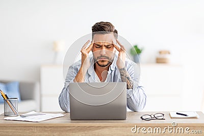 Deadline stress concept. Exhausted man tired after working on laptop, massaging temples, sitting at home office Stock Photo