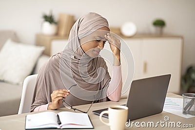 Deadline stress. Exhausted black woman in hijab tired after working on laptop for too long, having headache at home Stock Photo