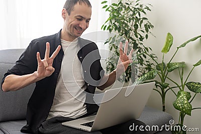 Deaf or hard hearing happy smiling young caucasian man uses sign language while video call using laptop while sitting on Stock Photo