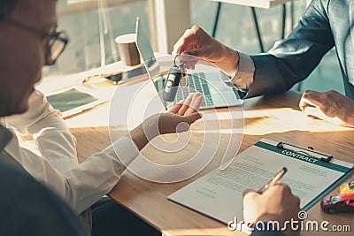 Dealer salesman giving car key to owner. client signing insurance document or rental car lease form Stock Photo