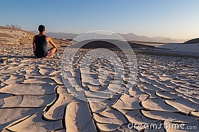 Death Valley - Man sitting on dry cracked clay crust at Mesquite Flat Sand Dunes in Death Valley National Park, California, USA Stock Photo