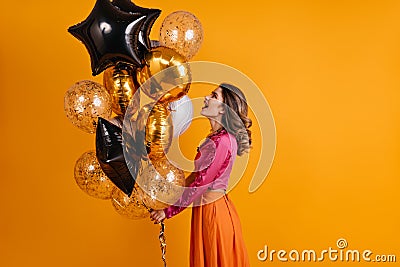 Debonair girl looking at party balloons. Indoor photo of pleased woman in pink blouse isolated on orange background Stock Photo