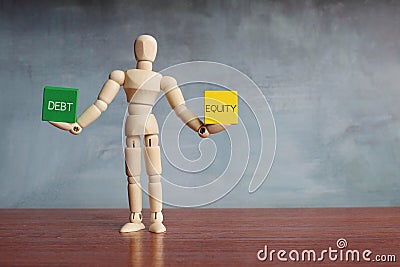 Wooden human figure balancing wooden cubes with text DEBT and EQUITY Stock Photo
