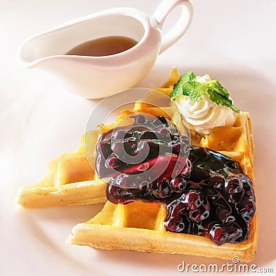 A decadent breakfast plate of Belgian waffles, whipped cream, and maple syrup. Stock Photo