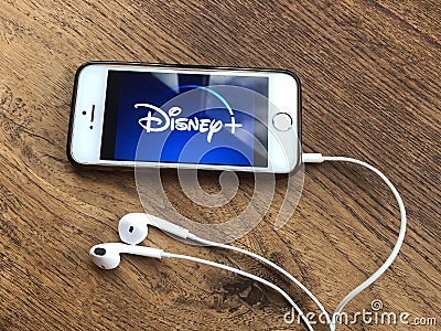December 2019 Parma, Italy: Disney + company logo icon on smarthone screen on wooden table with headphones. Disney + streaming vid Editorial Stock Photo