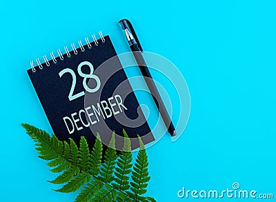 December 28th. Day 28 of month, Calendar date. Black notepad sheet, pen, fern twig, on a blue background Stock Photo