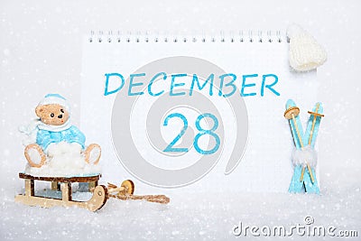 December 28th. Teddy bear sitting on a sled, blue skis and a calendar date on white snow. Day 28 of month. Stock Photo