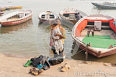 December 17.2019 Varanasi, India. A smiling mother holds a child wrapped up after swimming in the Ganges river. In the background Editorial Stock Photo