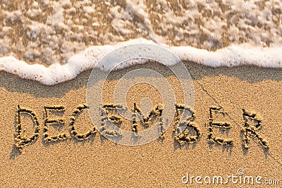 December - word drawn on the sand beach with the soft wave. Stock Photo