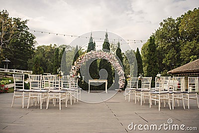 wedding ceremony in a restaurant garden: floral arch and rows white chairs Stock Photo