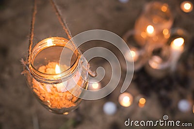 Decorated romantic place for a date with jars full of candles hunging on tree and standing on a sand. Copy Space Stock Photo