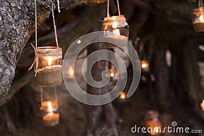 Decorated romantic place for a date with jars full of candles hunging on tree and standing on a sand. Copy Space Stock Photo