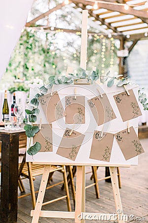 Decorated seating plan for wedding guests in woodent tent restaurant outdoors. Original rustic wooden board with guest Stock Photo