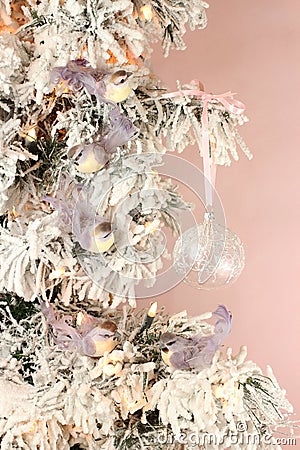 Decoration on Christmas tree - light violet birds and glassy ball on snowy spruce against pink background. Closeup Stock Photo