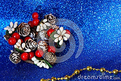 Decoration in the form of branches and berries of a holly as well as snowy Christmas tree cones. Sparkling blue background and Stock Photo