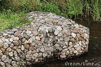 Decorative blocks with pebbles in mesh on calm pond bank Stock Photo