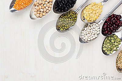 Decorative border of assortment different beans in spoons with copy space on white wood background. Stock Photo