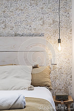 Decorative detail of a bedroom with a white painted wooden headboard, common incandescent lamp socket and fabric cushions Stock Photo