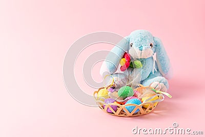 Decorative Easter eggs with feathers in basket and soft toy rabbit on pink background. Easter composition, greeting card with Stock Photo