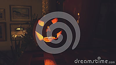Decorative, Halloween pumpkin statue with lit candle glowing in the dark on the shelf in living room Stock Photo