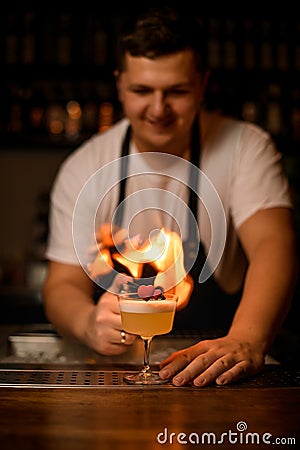 decorative heart on glass with foamy cocktail on the bar and male bartender with fire on background Stock Photo