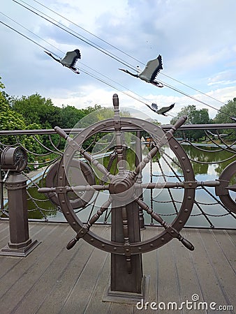 Decorative helm of a ship on a bridge in a park. Decorative metal flying cranes Stock Photo