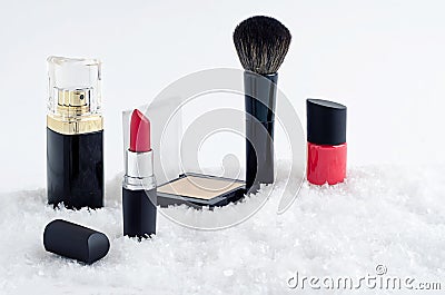 Decorative luxury cosmetics, red lipstick, powder, brush, nail polish and perfume on snow background Stock Photo