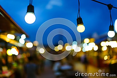 Decorative outdoor string lights bulb hanging on electricity post in street night market at night time. Stock Photo