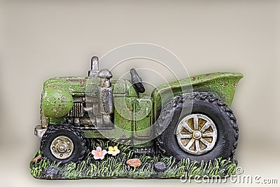 Decorative pretty farm ceramic planter shaped like a vintage green tractor sitting of grass with flowers - blurred background Stock Photo