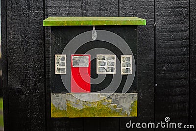 Decorative small black wooden postbox in shape of house with white windows and red door. Black wooden background Stock Photo