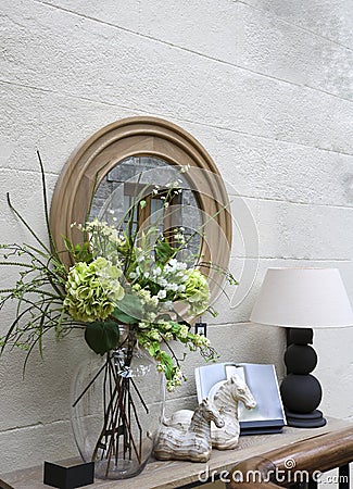Decorative wall decoration: a mirror, a console with a lamp, flowers and trinkets. Stock Photo