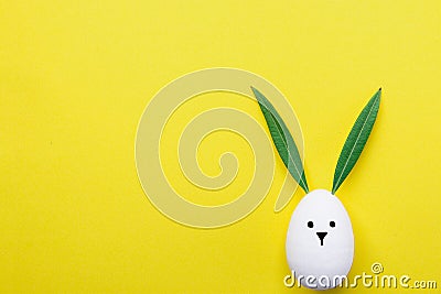 Decorative White Painted Easter Egg Bunny with Drawn Cute Kawaii Face. Green Leaves as Ears. Pastel Yellow Background. Spring Stock Photo