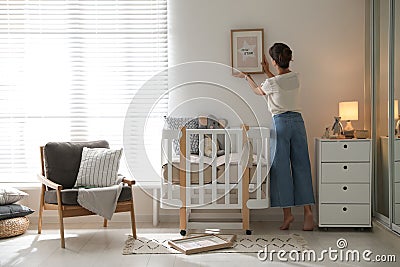 Decorator hanging picture on wall in baby room. Interior Stock Photo