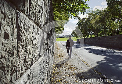 Deep perspective along a stone wall and a man walking in an autumn street. Stock Photo