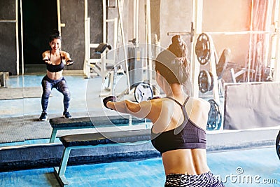 Deep squat of young beautiful woman in sportswear doing squat while standing in front of glass at gym Stock Photo