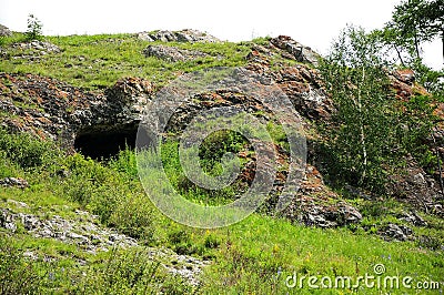 A deep stone cave and an entrance to it from the end of a low hill Stock Photo