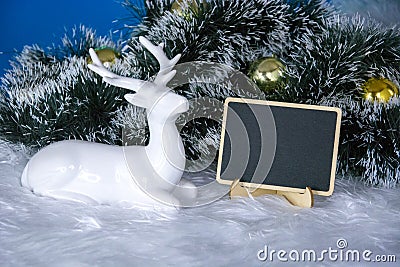 Deer in new year`s decor. A spruce branch with Golden Christmas balls and a sign for writing text. Design blank for greetings Stock Photo