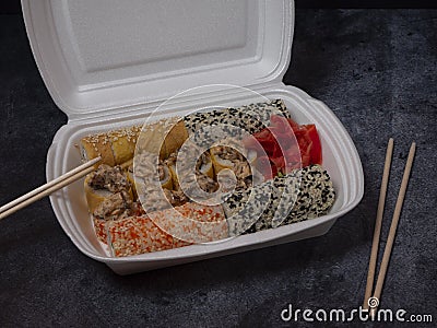 Defferent type of rolls or sushi set in a white plastic take-away box with chopsticks on gray stone table Stock Photo