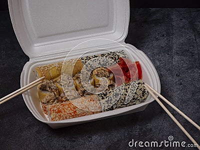 Defferent type of rolls or sushi set in a white plastic take-away box with chopsticks on gray stone table Stock Photo