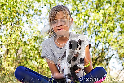 Defocus blonde little girl holding and caress cat, black and white small beautiful kitten. Nature green summer Stock Photo