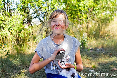 Defocus blonde little smiling girl holding and caress cat, black and white small adorable kitten. Nature green summer Stock Photo