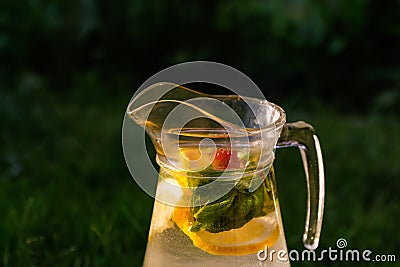 Defocus glass jug of lemonade with slice lemon, strawberry and mint on natural green background. Pitcher of fresh cold Stock Photo