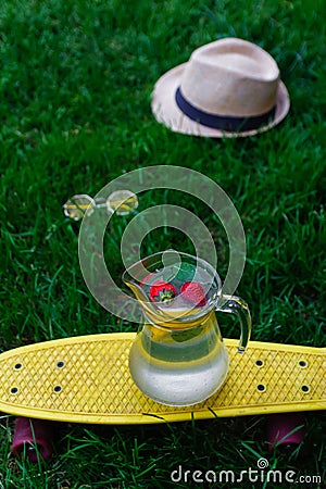 Defocus glass jug of lemonade with strawberry, slice lemon and leaves of mint on yellow board. Blurred grass background Stock Photo