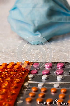 Defocus metaphor of a face in a blue medical mask looks at blisters of different pills. Virus and pandemic, quarantine Stock Photo