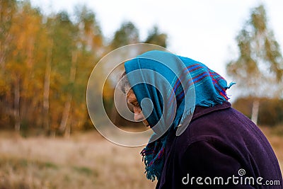 Defocus portrait of russian grandmother senior old woman standing in yellow autumn park. Old women in coat and shawl Stock Photo