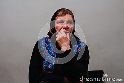 Defocus portrait of 60s russian grandmother senior old woman seating indoors. Old women in shawl. Sad thinking person Stock Photo