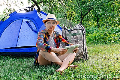 Defocus young woman working on tablet near camping tent outdoors surrounded by beautiful nature. Freelance, sabbatical Stock Photo